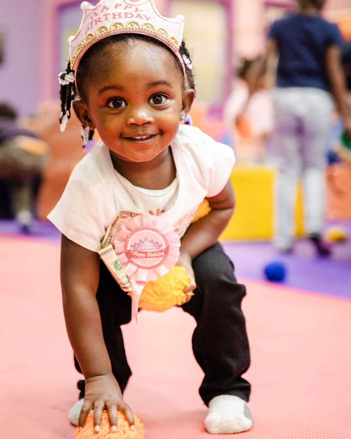 A toddler in a white shirt smiling at the camera, contact us today for toddler activities in Westbury.