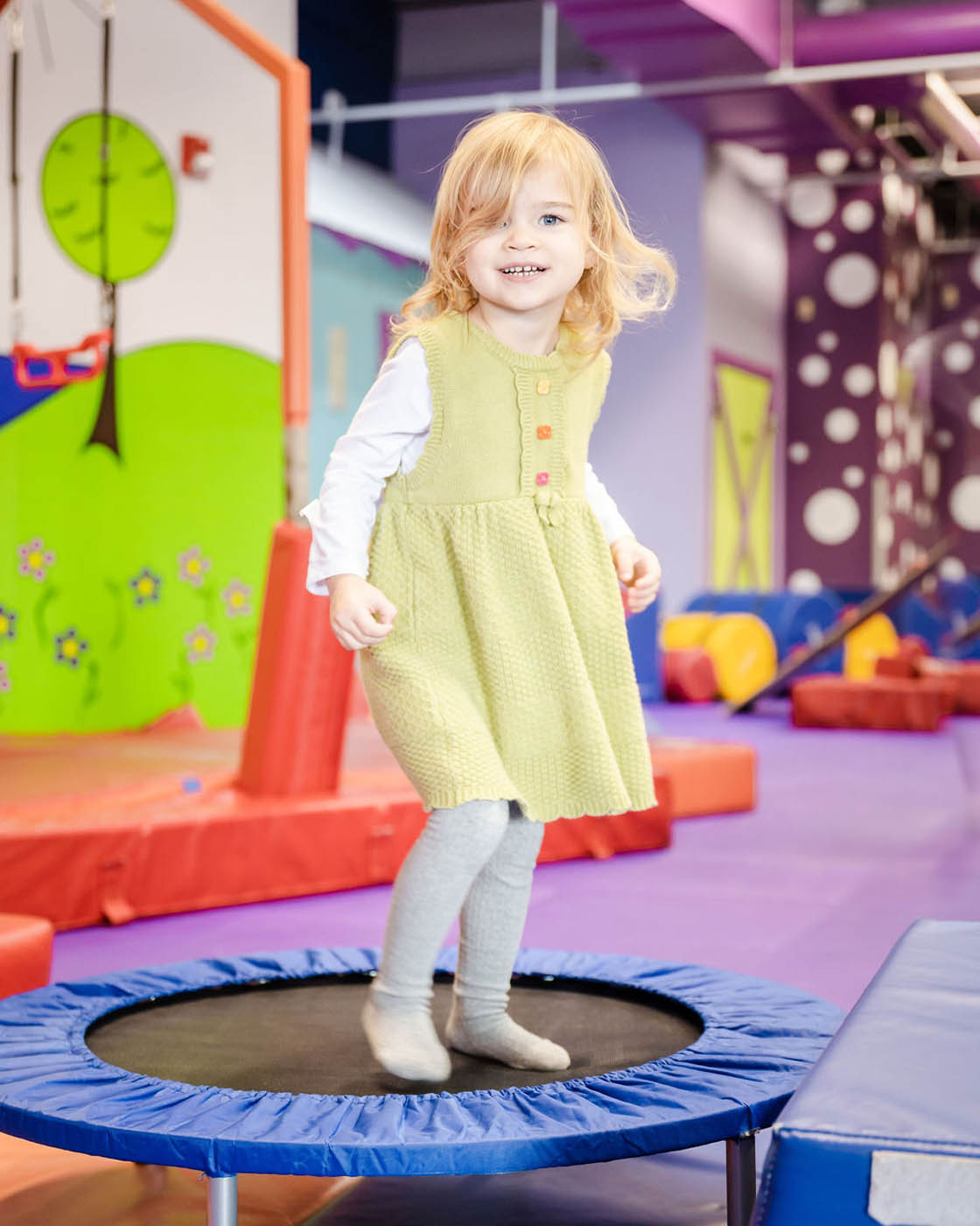 A little girl in a green dress playing on Romp n' Roll's gym equipment, contact us today for indoor kids activities in Willow Grove, PA.