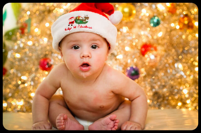 A cute baby in front of a Christmas tree - contact Romp n' Roll in St. Petersburg, FL for easy holiday preschool activities!