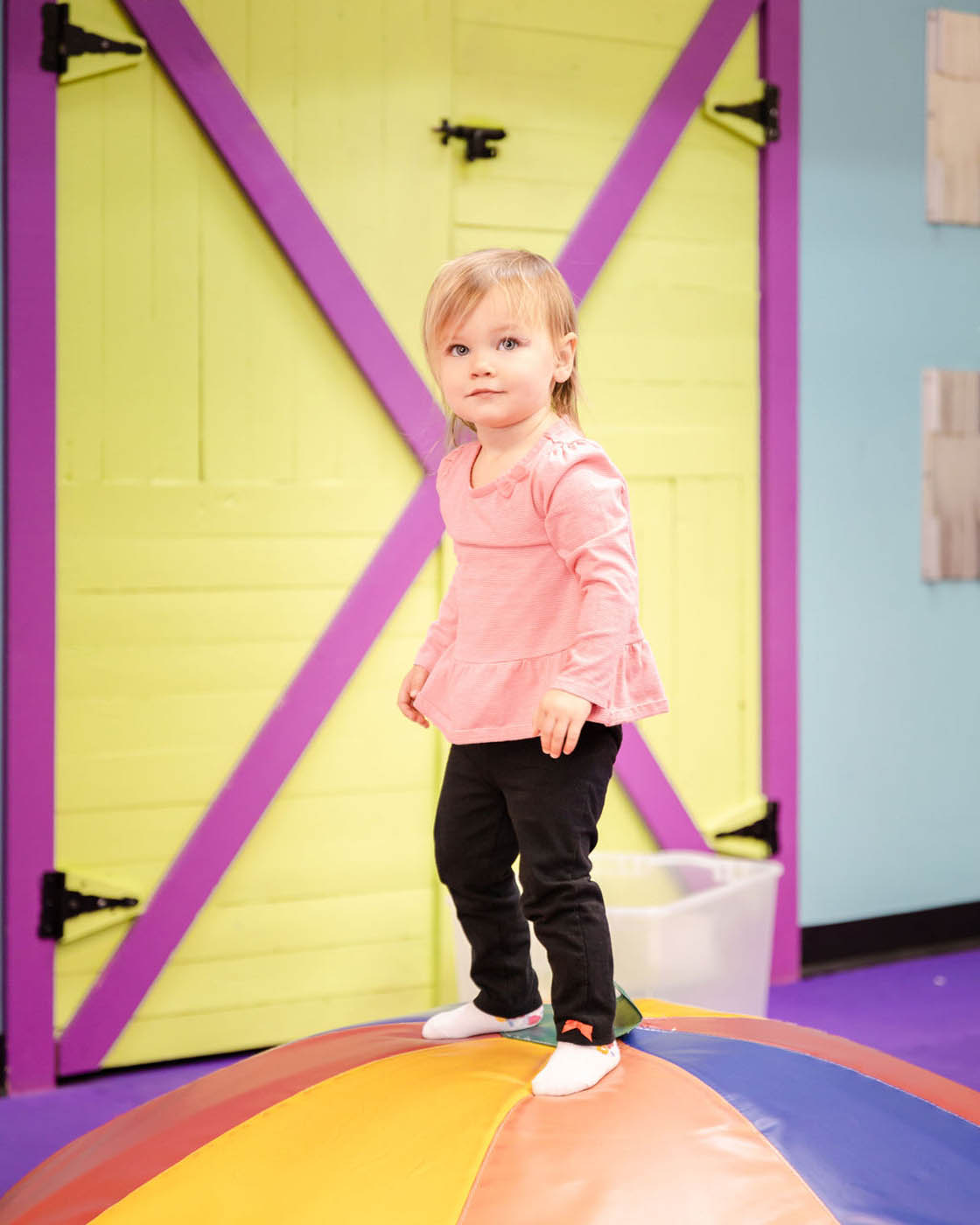 A girl standing on top of some mats used for gymnastic classes for 2 year olds in Raleigh, NC at Romp n' Roll.