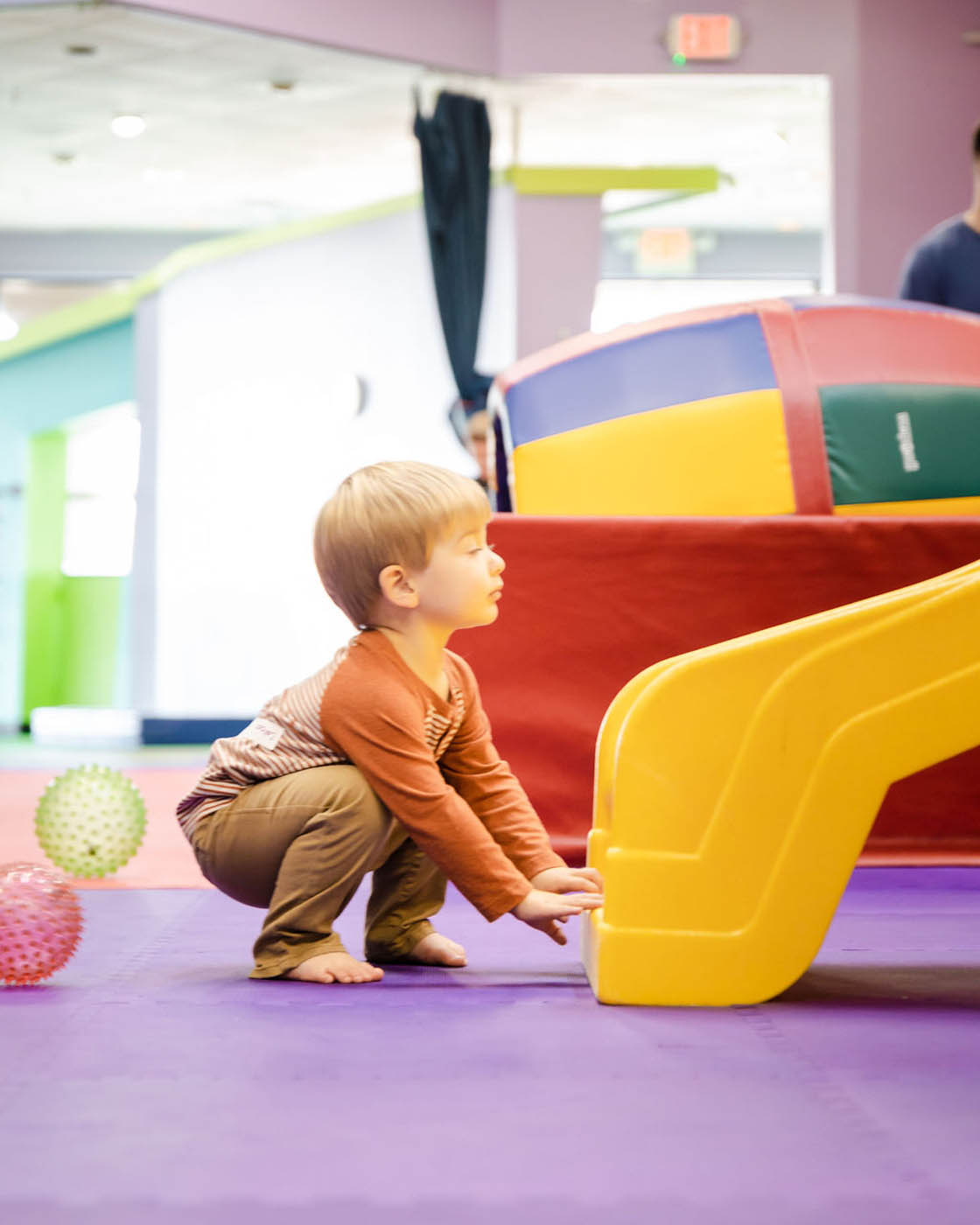 A young kid holding onto a yellow slide at Romp n' Roll - our kid-safe indoor playground franchise.