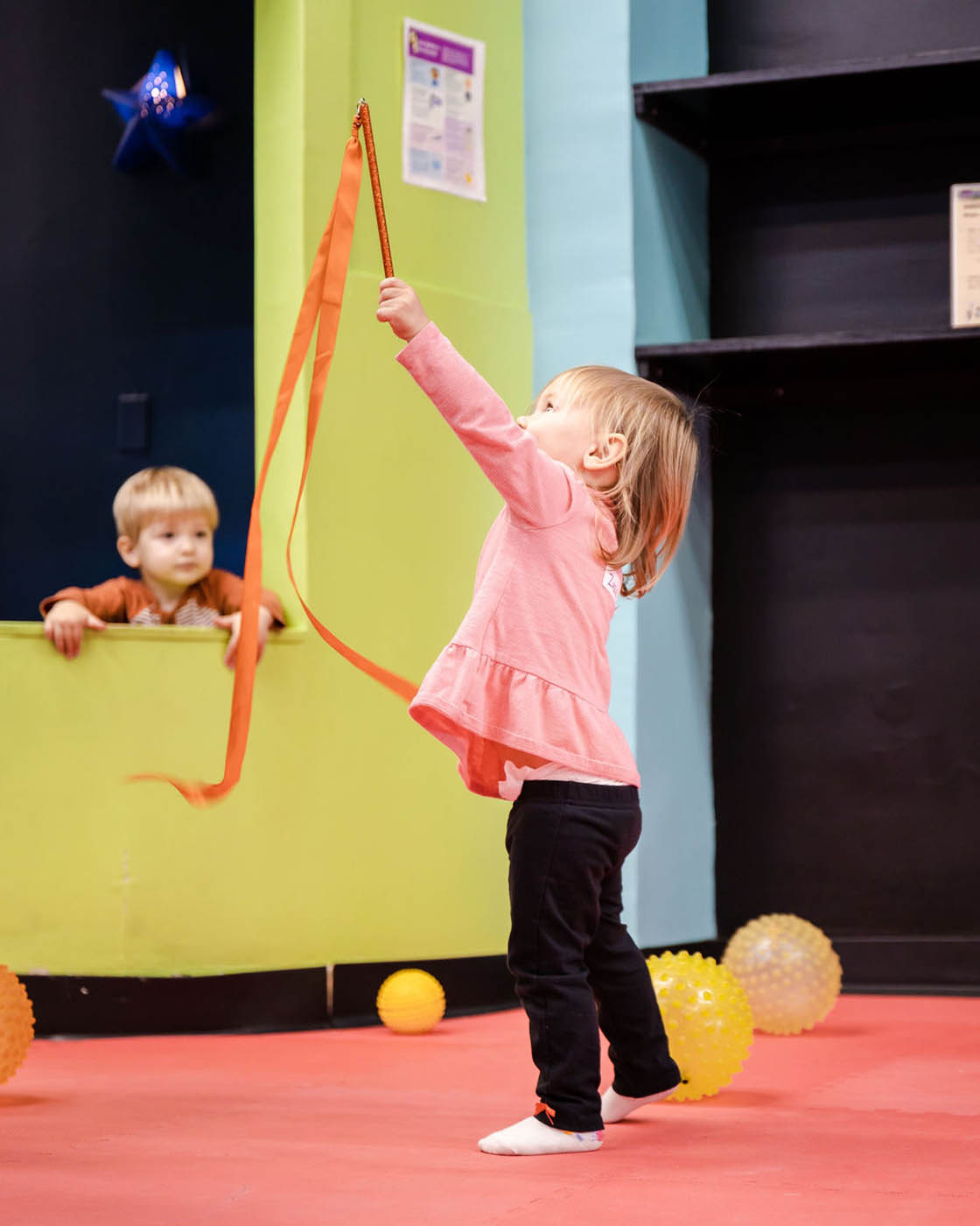 A little girl playing with ribbons and increasing her motor skills in sports classes with Romp n' Roll Katy.