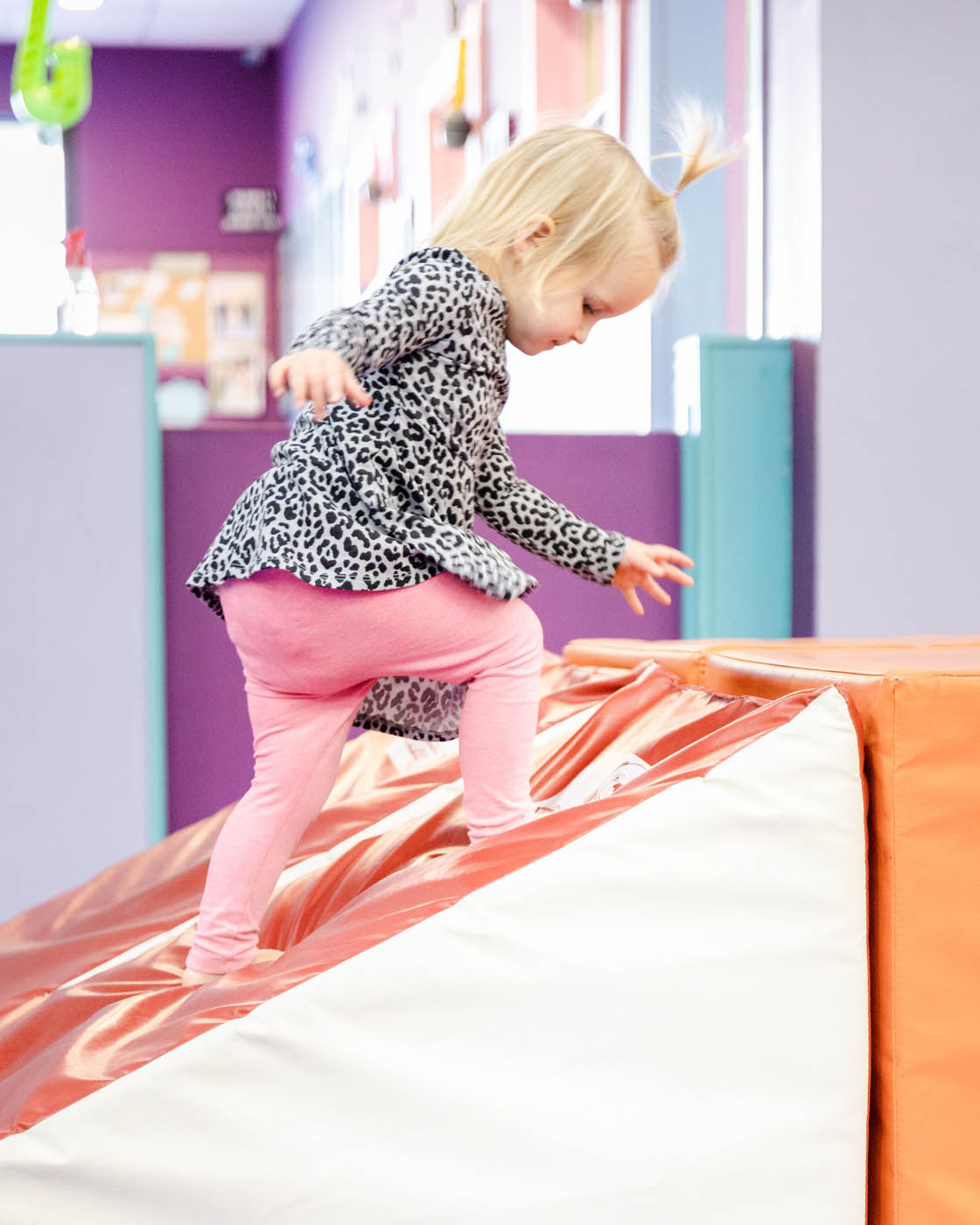 A girl climbing on soft gym equipment for gymnastics for 2 year olds.