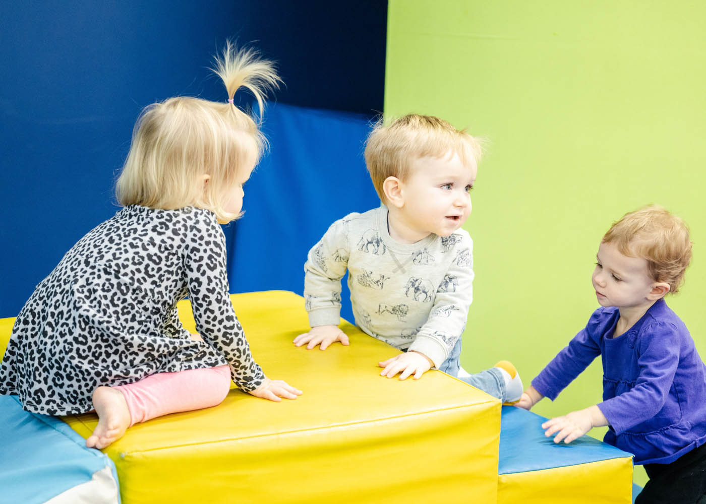 A three children crawling around at a Romp n' Roll kids gym franchise.