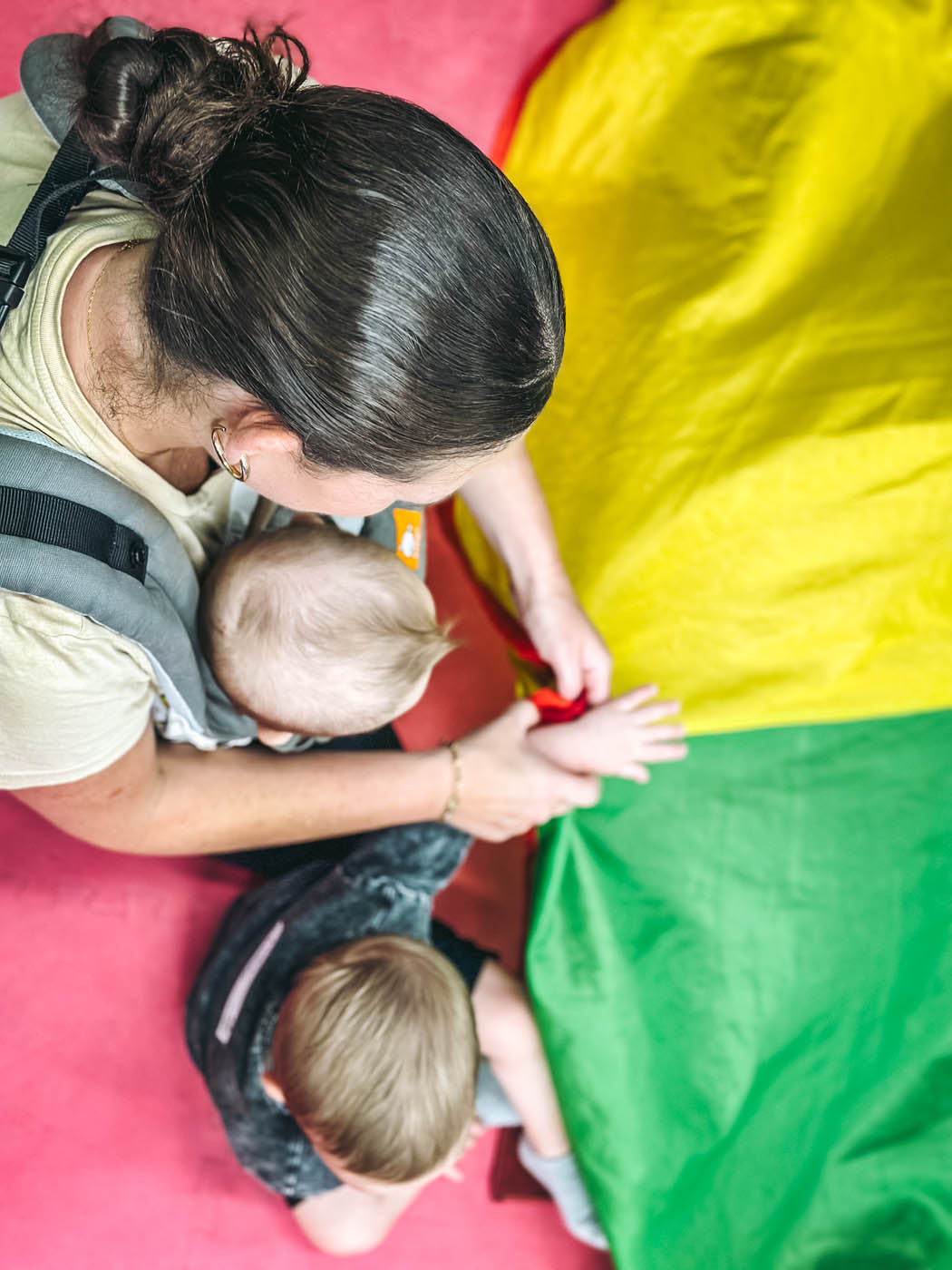 An adult with two kids playing with a colorful parachute at Romp n' Roll in St. Petersburg, FL.