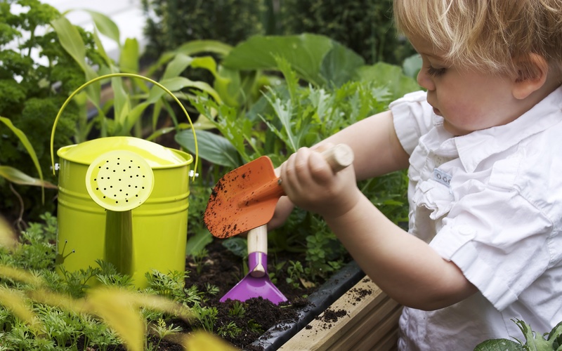 Child gardening with garden tools outside.