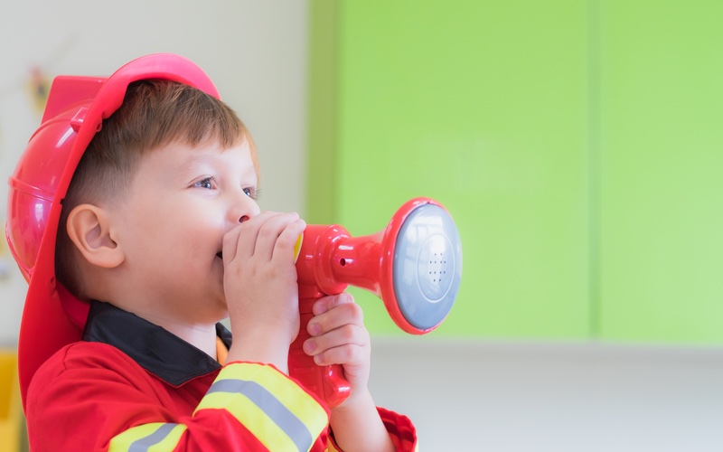 A boy dressed up in a firefighter costume - perfect for adventure play at Romp n' Roll West End toddler birthday parties.
