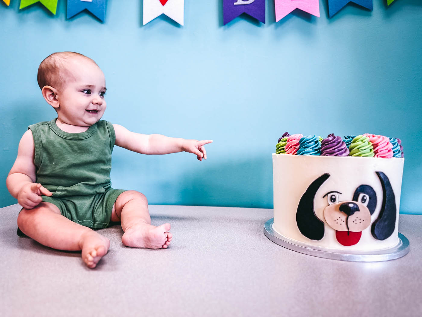 A little baby boy sitting next to a Rompy cake, book a birthday party in Raleigh, NC!