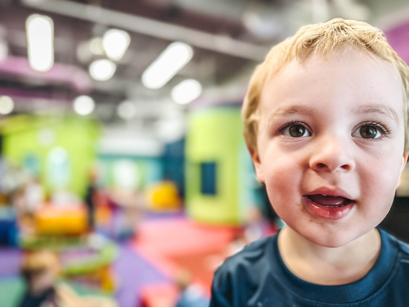 A little boy with blonde hair smiling and playing in Romp n' Roll Pittsburgh's gym.