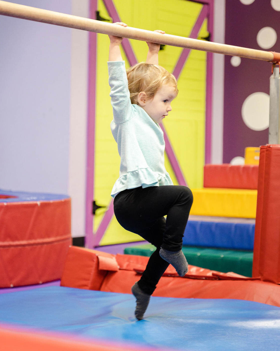 A kid swining from Romp n' Roll gym equipment - safe kids fitness classes in Charlotte, NC.