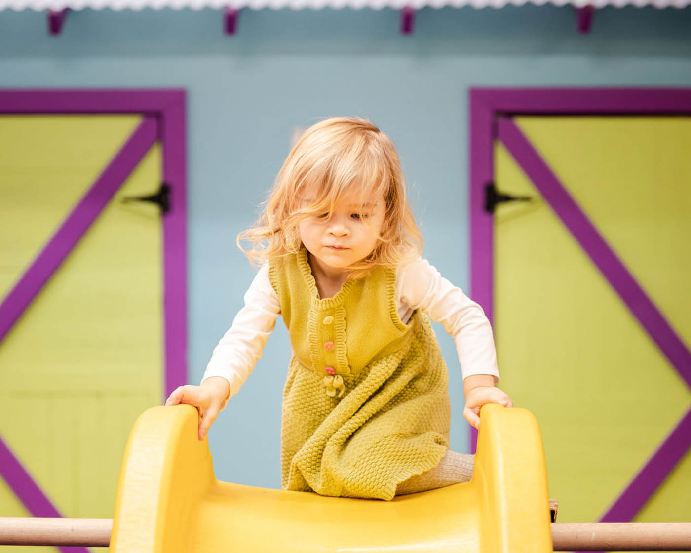 A toddler playing on a yellow slide at Romp n' Roll Midlothian's classes for 3 year olds in Midlothian, VA