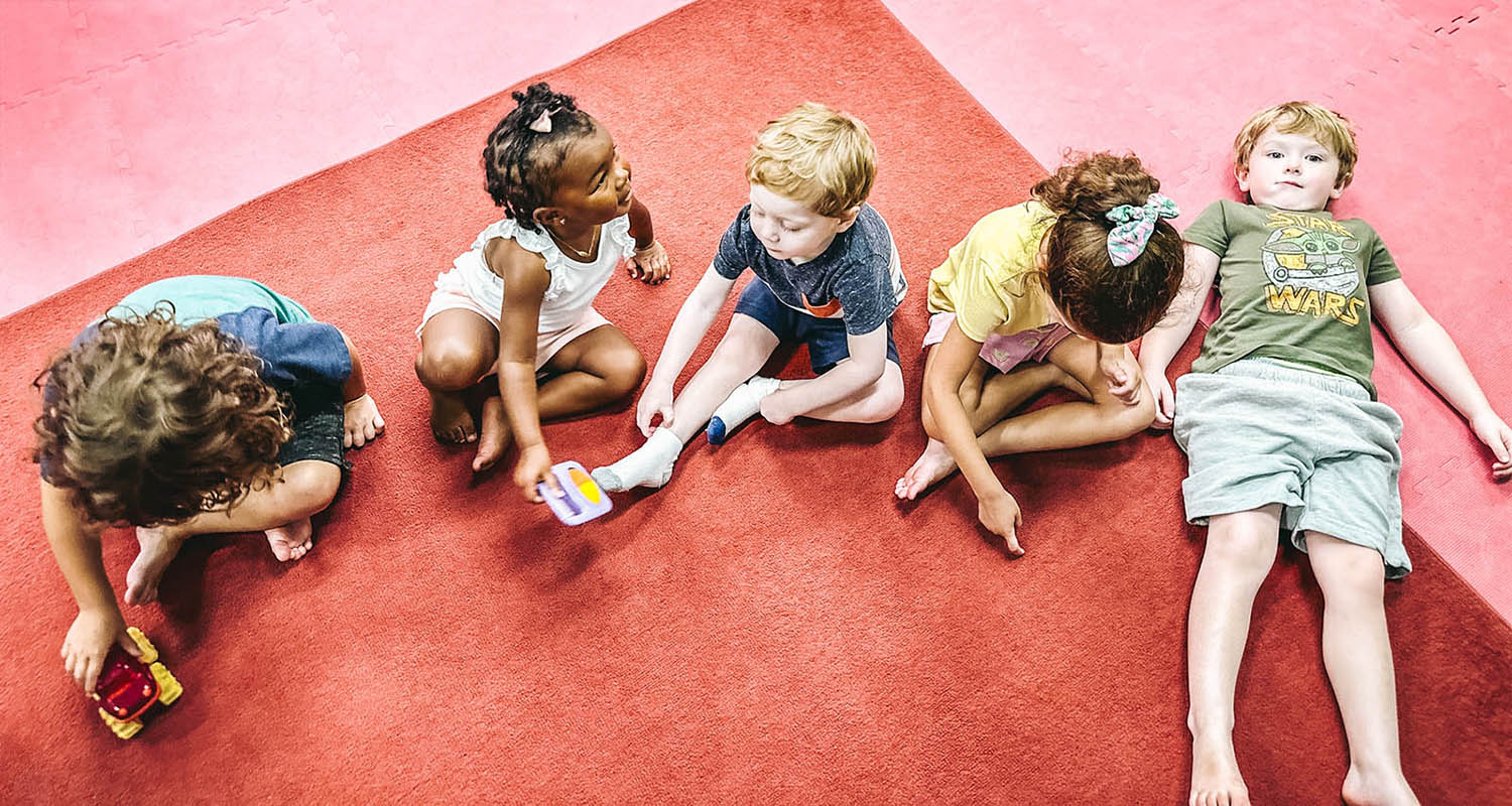 A group of kids sitting on the floor at a Romp n' Roll facility.