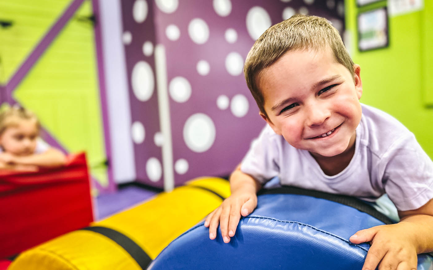 A little boy smiles at the camera as he plays on a soft piece of gym equipment at Romp n' Roll.