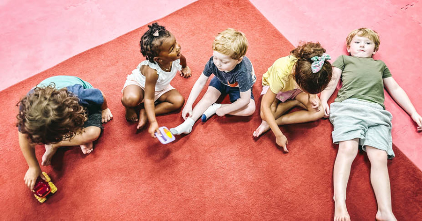 A group of kids sitting on the floor at a Romp n' Roll facility enjoying mixed age classes for kids in St. Petersburg, FL.