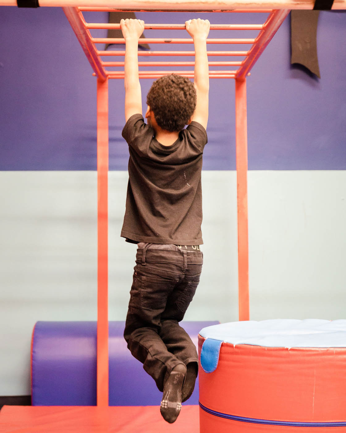A boy hanging from monkey bars on kid-safe gym equipment at Romp n' Roll in Raleigh.
