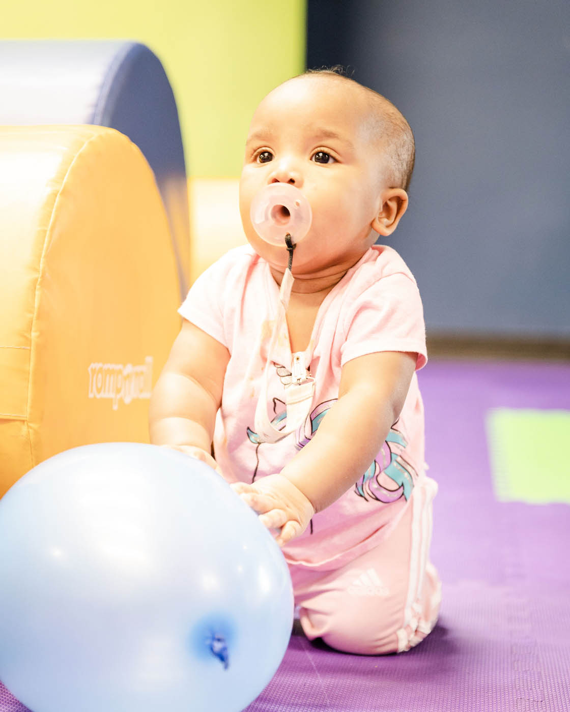 A baby in a gym class working on basic motor skills and enjoying playing with a blue ball - Romp n' Roll.