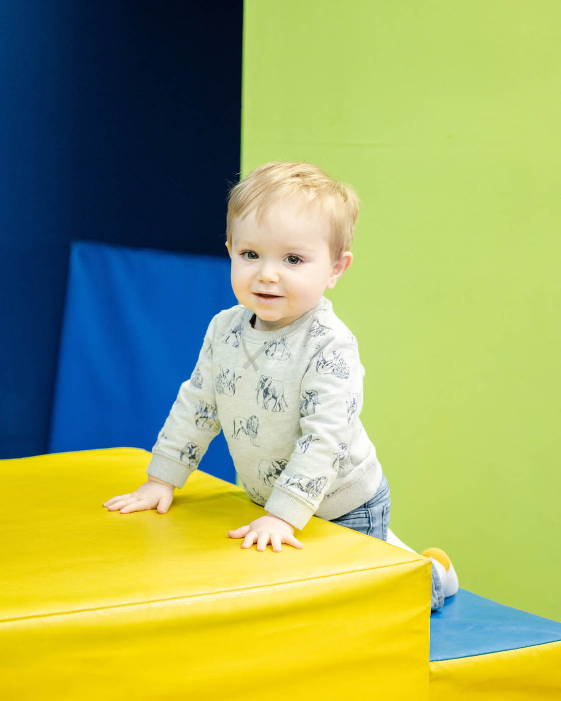 A young boy climbing on some age appropriate gym equipment at a Charlotte toddler tumbling class.
