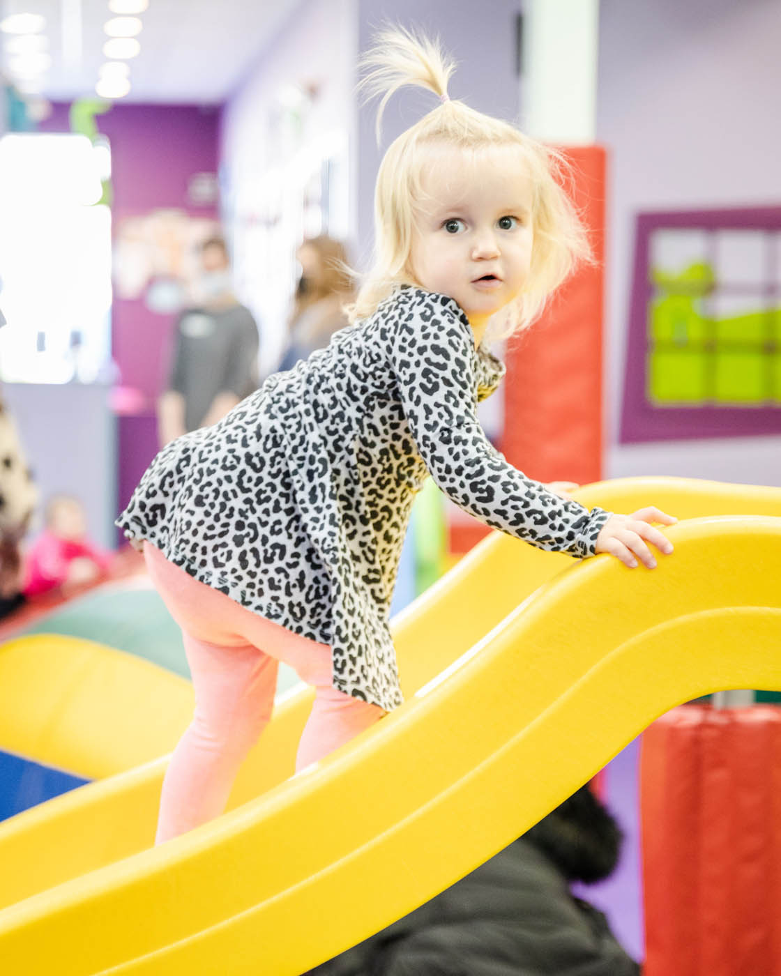 A little girl climbing up a yellow slide at Romp n' Roll.