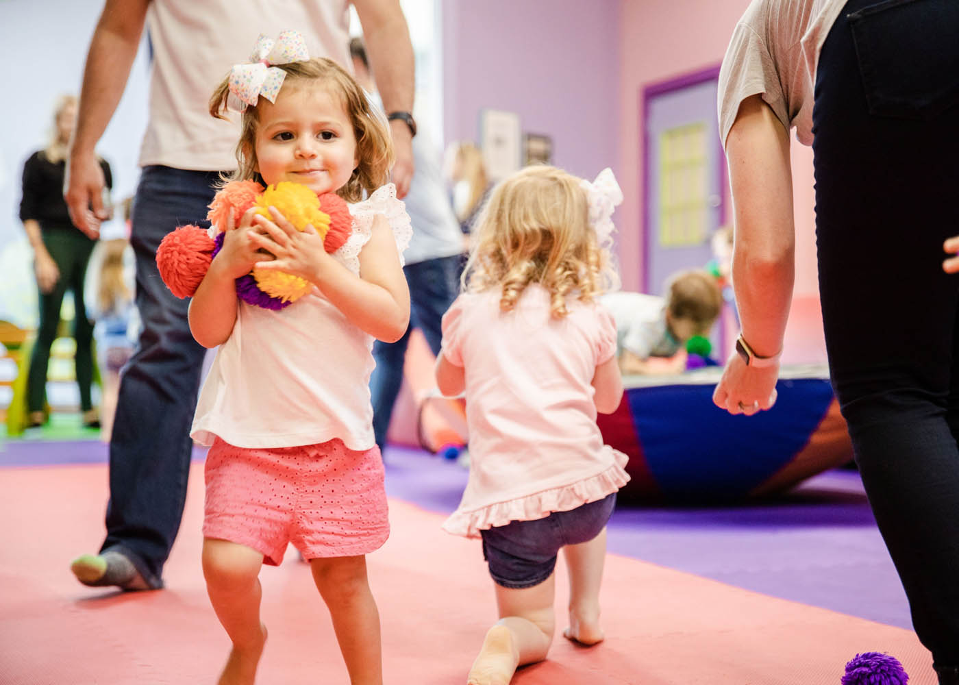 A little girl holding an armful of plush toys and having fun at a Romp n' Roll class.