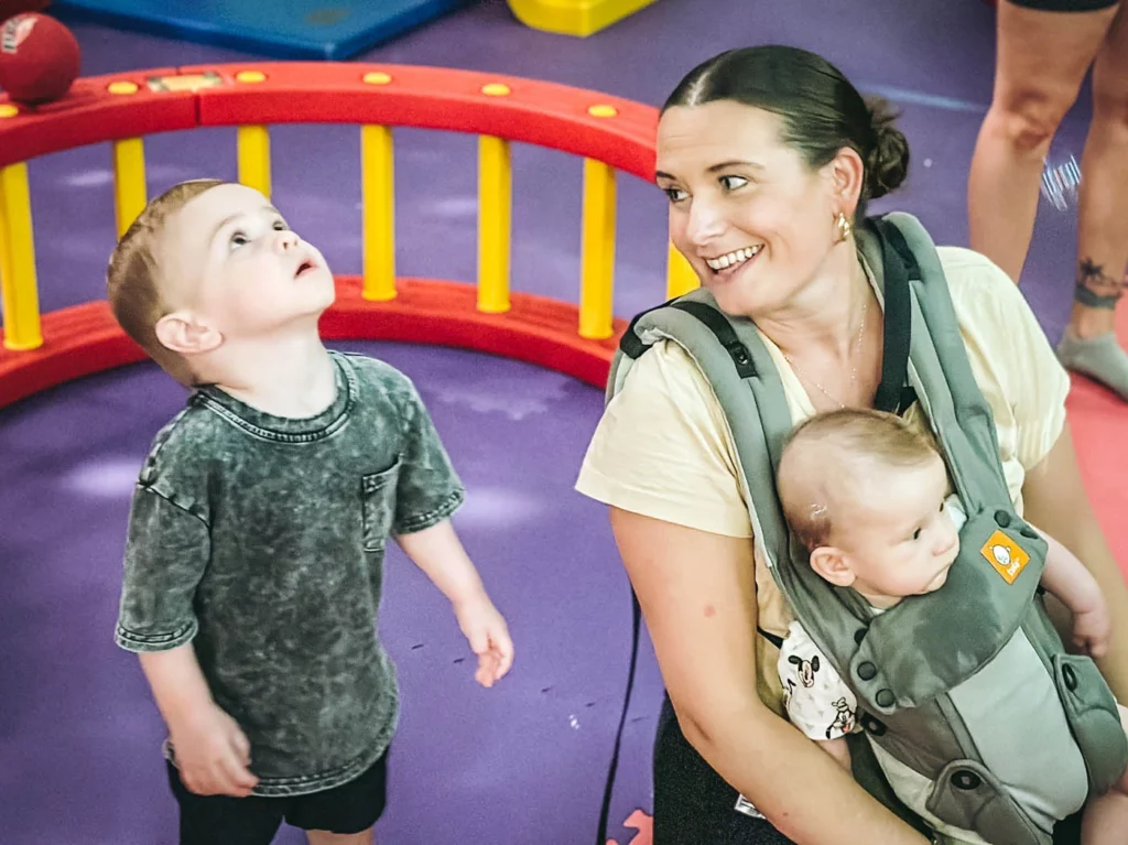 An adult holding a baby and a younger boy standing next to her - join our preschool classes today.